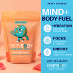 A stand-up pouch of EveryBody Everyday Stick drink mix in Peach Hibiscus flavor, shown next to a blue informational panel listing benefits like hydration, focus, and energy. The pouch is peach-orange with a cartoon globe logo, and the background is a soft peach-pink with scattered flower petals.
